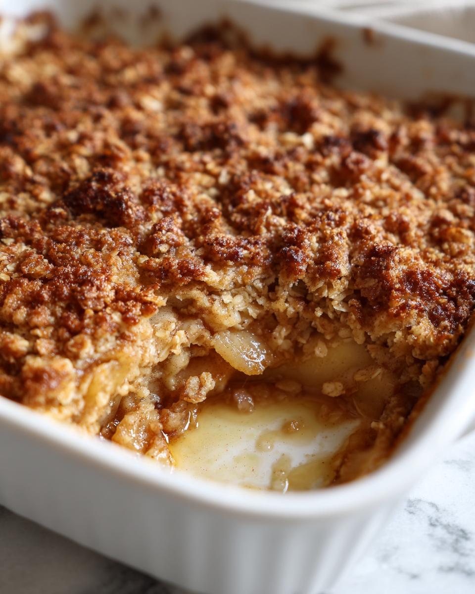A close-up view of a scoop removed from a baked apple crisp, showing the gooey apple filling and crunchy oat topping.