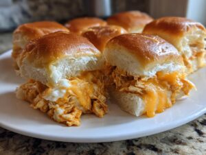 Close-up of cheesy buffalo chicken sliders on a white plate, showing shredded chicken and melted orange cheese.