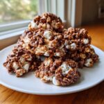 A stack of gooey, no-bake avalanche cookies made with chocolate, popcorn, and marshmallows, sitting on a white plate.