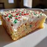 Close-up of a single serving of christmas sugar cookie bars with thick white frosting and red and green sprinkles.