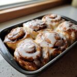 Close-up of freshly baked cinnamon rolls with heavy cream glaze in a baking pan.
