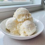 Three generous scoops of creamy, white cottage cheese ice cream served in a white bowl.