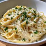 Close-up of creamy spaghetti coated in sauce, topped with grated parmesan and fresh parsley, representing the garlic parmesan pasta recipe.