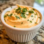 Close-up of creamy, orange-hued remoulade sauce topped with fresh chopped parsley in a white fluted bowl.