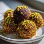 Close-up of several golden and dark dubai chocolate balls wrapped in crispy pastry and topped with crushed pistachios.