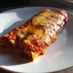 Two rolled easy chicken enchiladas covered in red sauce and melted cheddar and Monterey Jack cheese on a white plate.