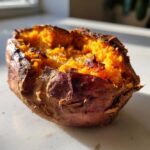 Close-up of a perfectly baked sweet potato split open, showing the bright orange, fluffy interior.