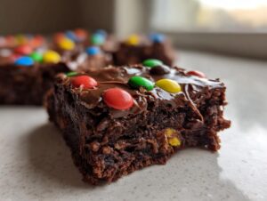Close-up of a fudgy cosmic brownies square with chocolate frosting and colorful candies, showing a bite taken out.