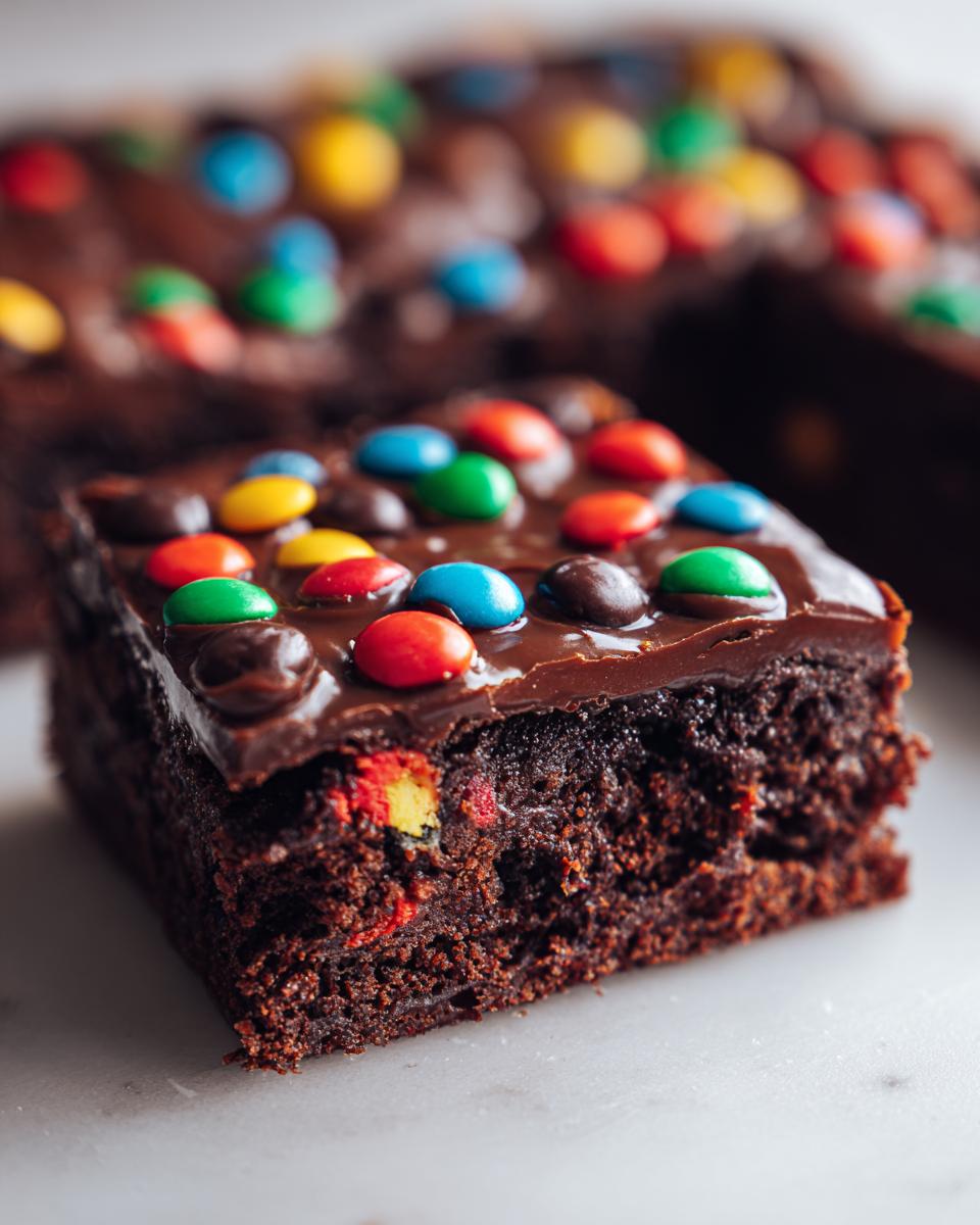 Close-up of a fudgy cosmic brownie slice topped with chocolate frosting and colorful candy-coated chocolates.
