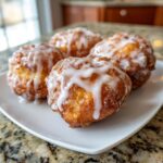 Four golden brown, freshly fried apple fritter dough balls drizzled generously with white vanilla glaze.