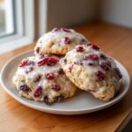 Three freshly baked cranberry orange cookies topped with a thick white glaze and dried cranberries.
