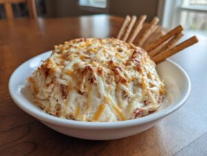 A bowl of hot, baked reuben dip topped with melted, browned cheese, served with breadsticks.