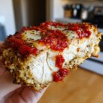 Close-up of a thick slice of keto chicken parmesan showing the juicy white meat, crispy crust, melted mozzarella, and bright red marinara sauce.