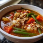 A close-up of a white bowl filled with rich Maryland crab soup, featuring large chunks of crab meat, carrots, and green beans.