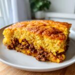 Close-up of a thick slice of Mexican cornbread casserole with a golden-brown top and savory ground meat filling.