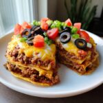 Two slices of layered Mexican pizza topped with melted cheese, black olives, tomatoes, and green onions.