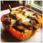 Close-up of a baked philly cheesesteak stuffed pepper topped with melted white cheese.