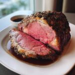 A beautifully cooked prime rib recipe roast, sliced to show a perfect medium-rare center with a herb crust, resting in its juices.