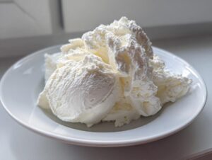 Close-up of scoops of white, creamy cottage cheese ice cream served on a small white plate.