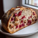 A thick slice of homemade cranberry walnut bread showing vibrant red cranberries and walnuts embedded in the airy crumb.