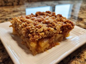 A close-up of a square slice of warm pear crisp featuring a thick, golden-brown oat crumble topping over soft, spiced fruit filling.