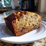 Close-up of a moist slice of vegan banana bread studded with chocolate chips on a white plate.