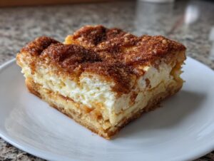 A close-up of a single square slice of sopapilla cheesecake showing the creamy filling and cinnamon sugar crust.