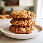 A stack of three golden brown oatmeal cookies resting on a small white plate.