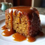 Close-up of a rich, moist slice of sticky toffee pudding recipe covered in dripping caramel sauce on a white plate.