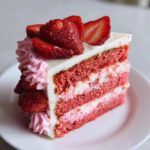 A beautiful slice of layered strawberry cake with white frosting and topped with fresh strawberries.