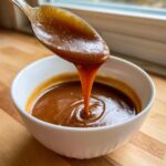 A spoonful of thick, rich homemade brown gravy dripping back into a white bowl.