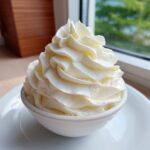 A close-up of perfectly piped, creamy vanilla buttercream frosting mounded high in a small white bowl.