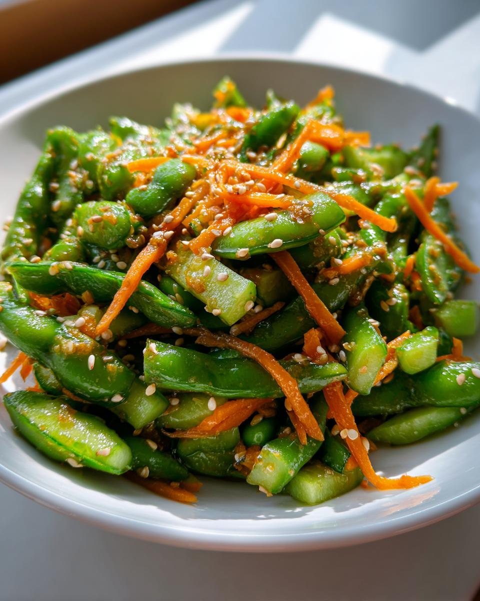 Close-up of a bright green edamame salad mixed with shredded carrots and topped with sesame seeds.