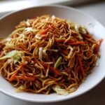 A close-up shot of a generous serving of savory fried noodles mixed with shredded carrots and cabbage.