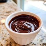 Close-up of thick, glossy homemade chocolate sauce swirled inside a small white ramekin.