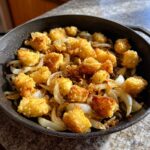 Golden brown, crispy fried potatoes mixed with caramelized onion slices in a dark cast iron skillet.