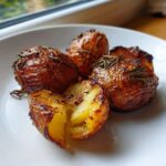 Close-up of four perfectly crispy roast potatoes seasoned with rosemary on a white plate.