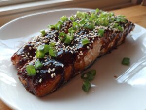 A perfectly cooked fillet of teriyaki salmon glazed with dark sauce, topped with sesame seeds and chopped green onions.