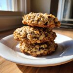 Three freshly baked banana oatmeal cookies stacked on a white plate, illuminated by natural sunlight.