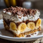A close-up of a rich slice of banoffee pie featuring a graham cracker crust, bananas, cream, and chocolate shavings.