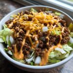 A close-up of a Big Mac Salad bowl featuring lettuce, seasoned ground beef, onions, shredded cheese, and special sauce.
