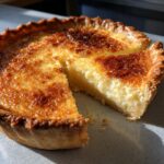 A whole buttermilk pie with one slice cut out, showing the creamy filling and golden-brown top.