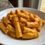 Close-up of rigatoni pasta coated in a rich, orange butternut squash pasta sauce, sprinkled with pepper.