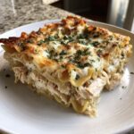 A close-up of a delicious slice of chicken alfredo lasagna with layers of pasta, shredded chicken, and melted cheese topping.