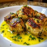 Close-up of golden brown chicken piccata meatballs resting in a bright yellow lemon butter sauce, garnished with parsley.