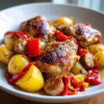 Close-up of crispy chicken scarpariello thighs served with roasted potatoes, sausage slices, and red peppers.