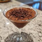 A creamy chocolate martini served in a coupe glass, topped generously with dark chocolate shavings.