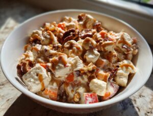 A bowl of creamy apple salad mixed with marshmallows, pecans, and drizzled with caramel sauce.