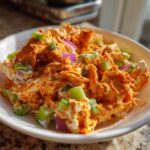 A close-up, appetizing shot of creamy buffalo chicken salad mixed with celery and red onion in a white bowl.
