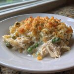 A close-up serving of creamy chicken noodle casserole with shredded chicken, peas, and a golden breadcrumb topping.